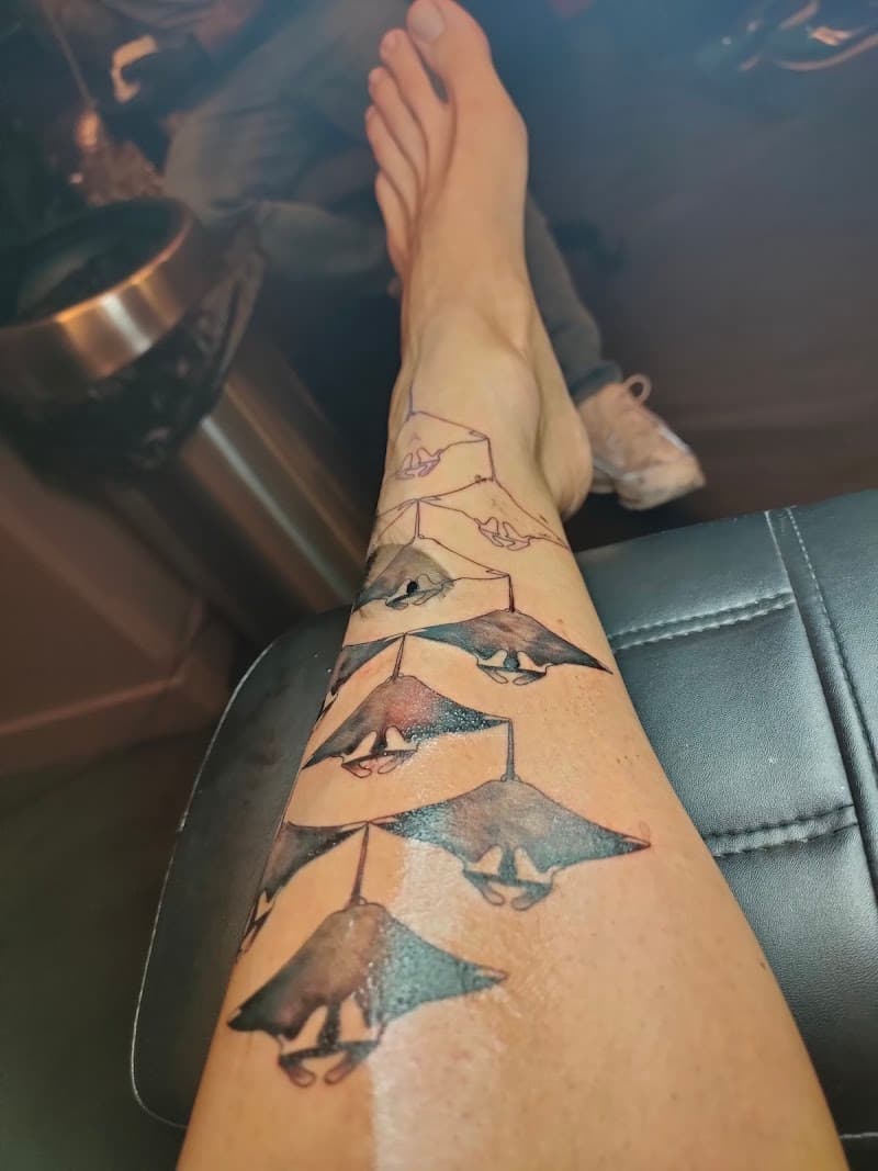 Tattoeage van een groep manta roggen op het onderbeen, deels ingekleurd.