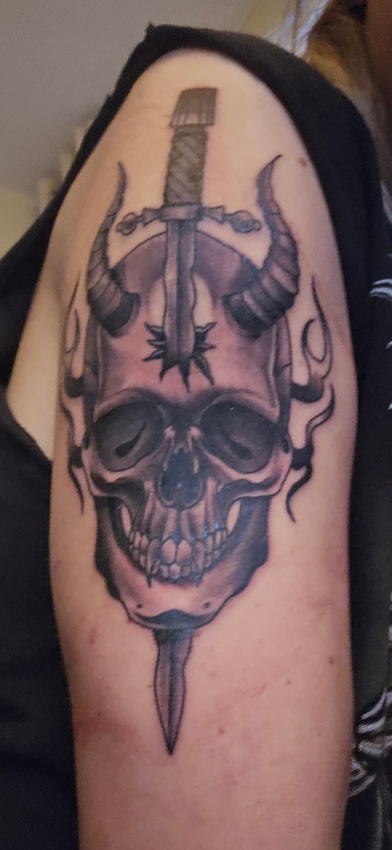 Schedel met hoorns en dolk tattoo op bovenarm.