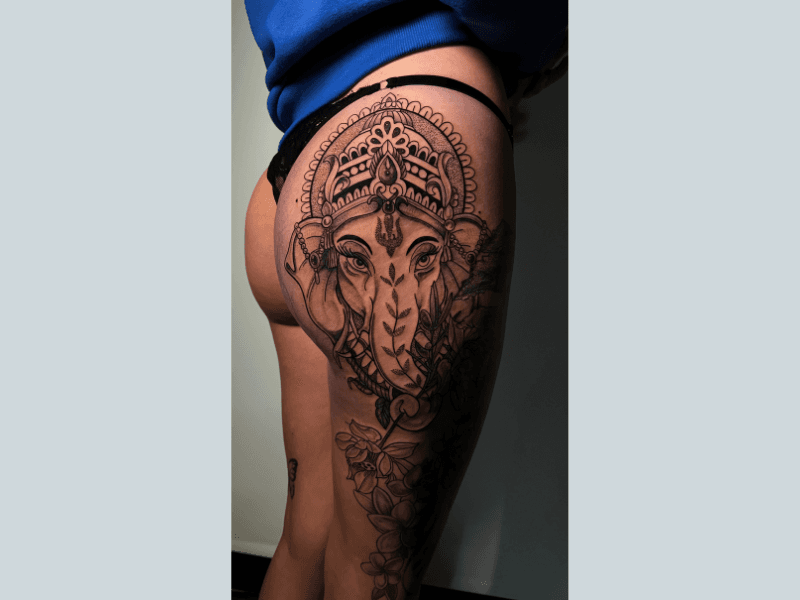 Grote Ganesha tattoo met bloemen op de heup en bovenbeen.
