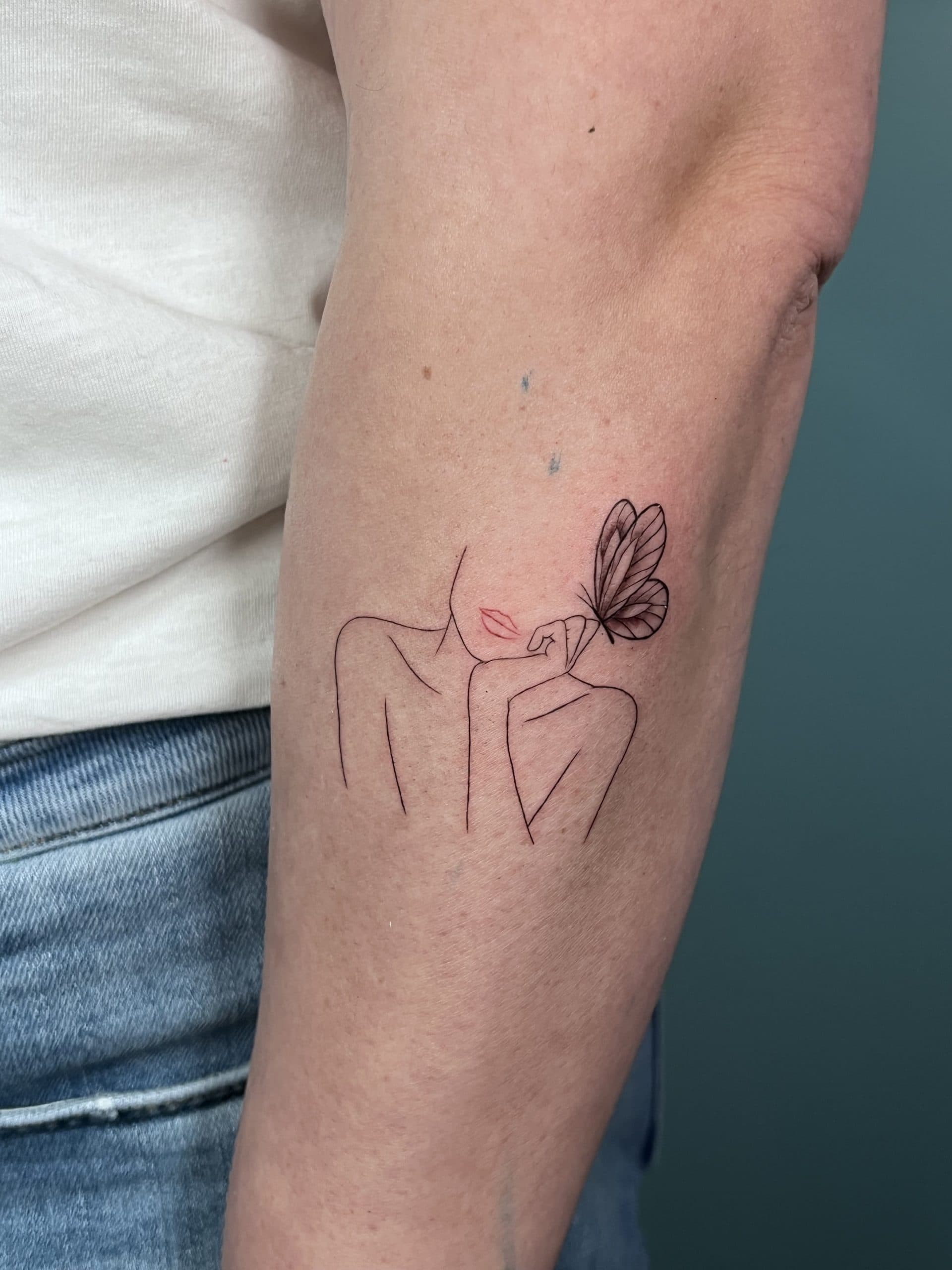 Fineline tattoo van een vrouw met een vlinder op haar hand.