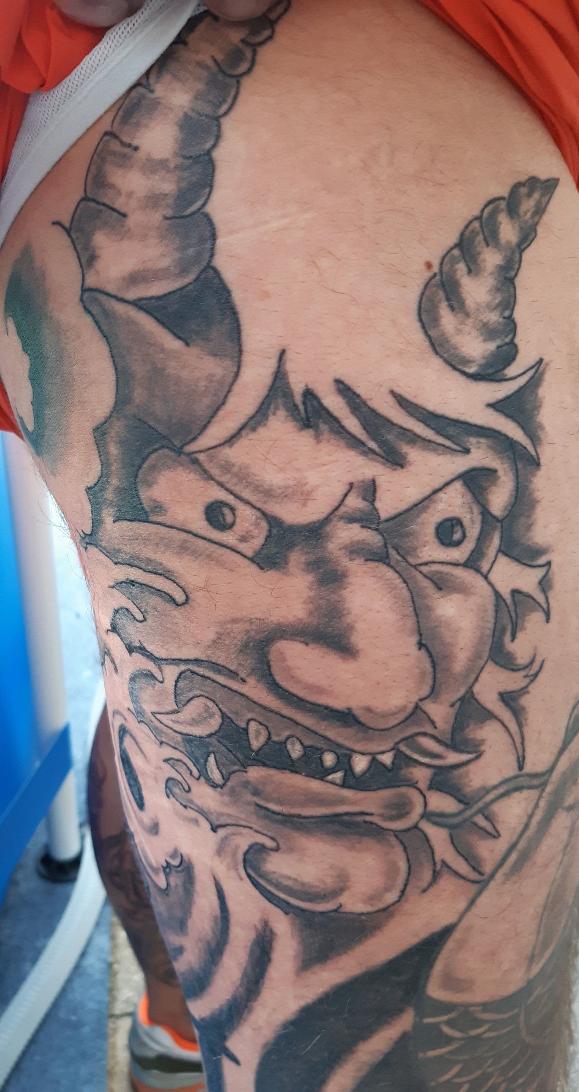 Zwart-wit Oni masker tattoo op het bovenbeen.