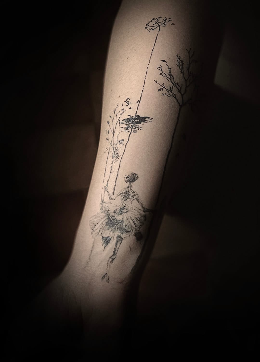 Schetsstijl tattoo van een ballerina op een schommel aan een boom.