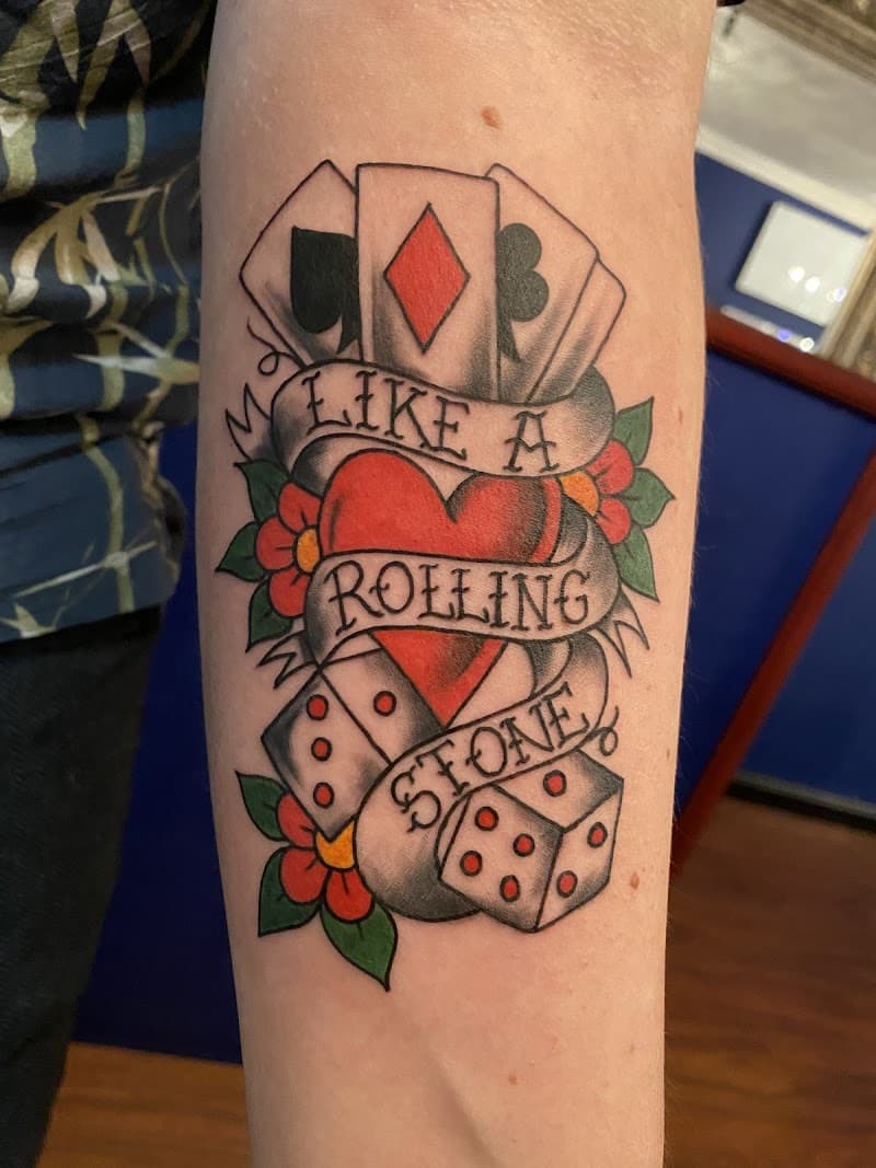 Traditionele tattoo met kaarten, hart, dobbelstenen en 'LIKE A ROLLING STONE' tekst.