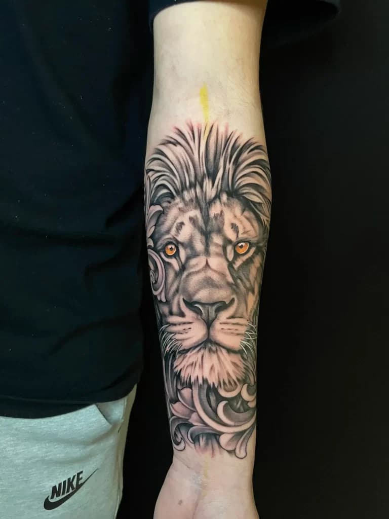 Realistische leeuwenkop met oranje ogen en sierlijke details op de onderarm.