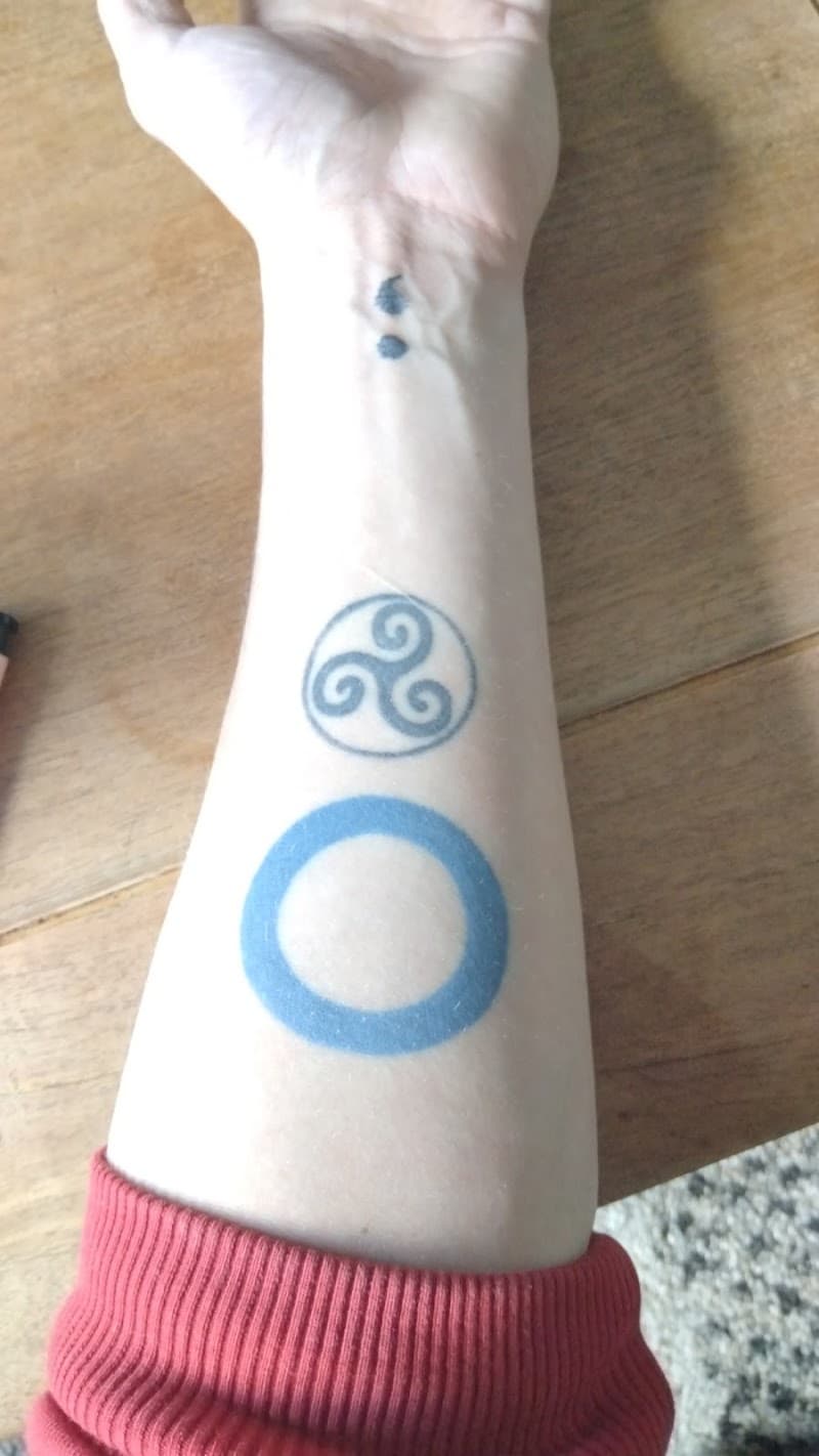 Drie kleine symbolen op onderarm: puntkomma, triskele en blauwe cirkel.