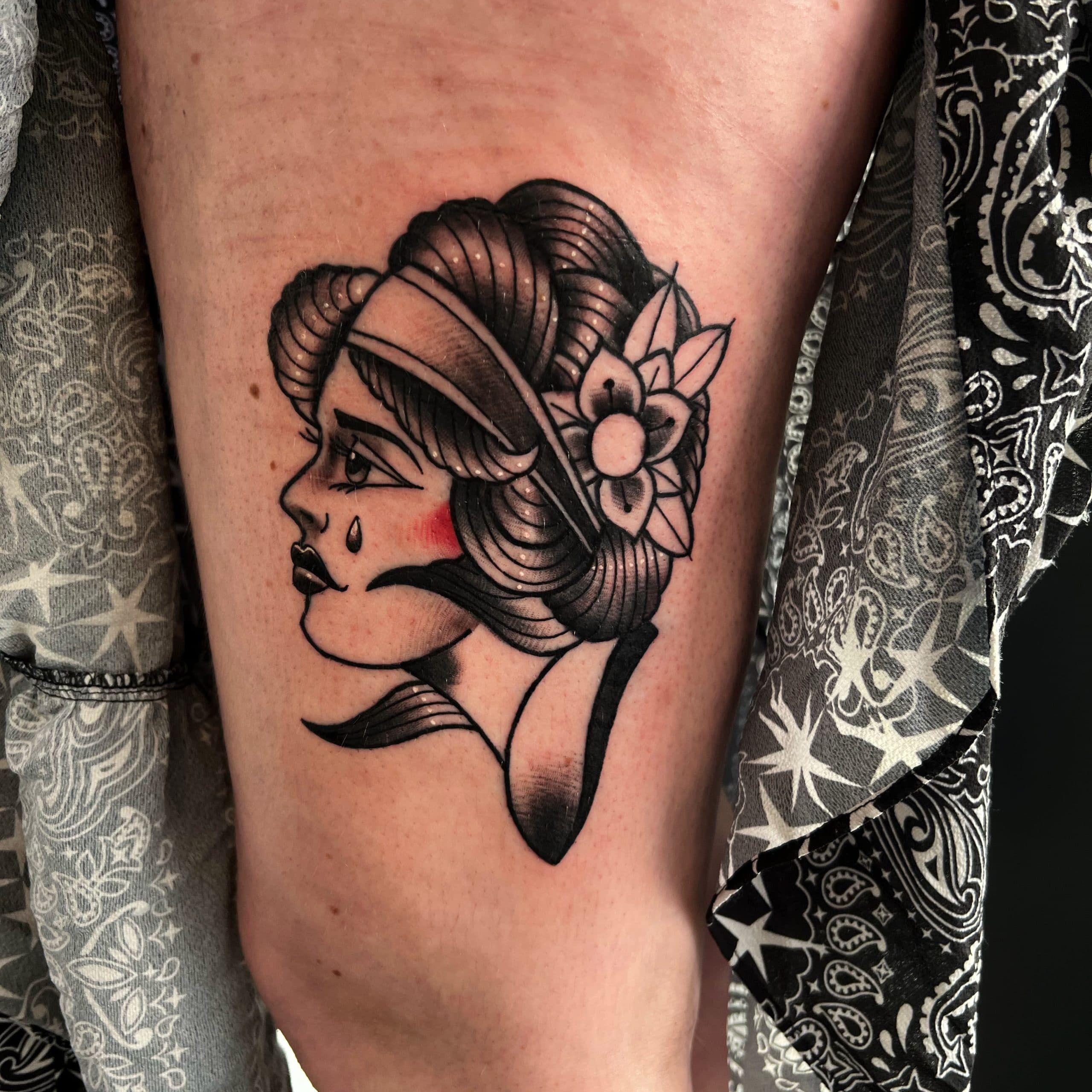 Traditionele tattoo van een huilende vrouw in profiel op het bovenbeen.