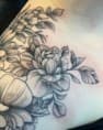 Fineline bloementattoo met pioenroos en bladeren op schouder.
