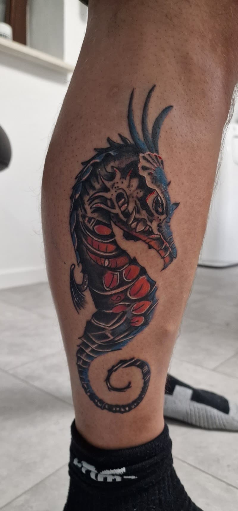 Donkere, biomechanische zeepaard tattoo op onderbeen.