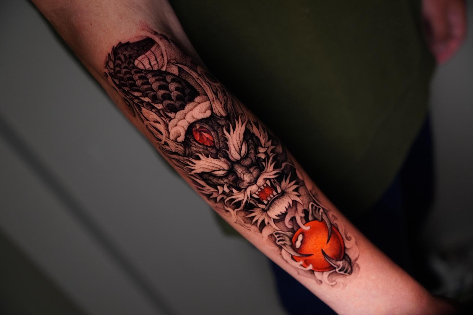 Gedetailleerde drakenkop met rode bol op onderarm.