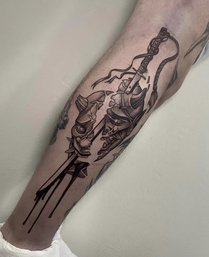 Gebroken Hannya masker met een zwaard erdoorheen op het onderbeen.