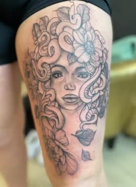 Blackwork Medusa tattoo met slangen en bloemen op bovenbeen.