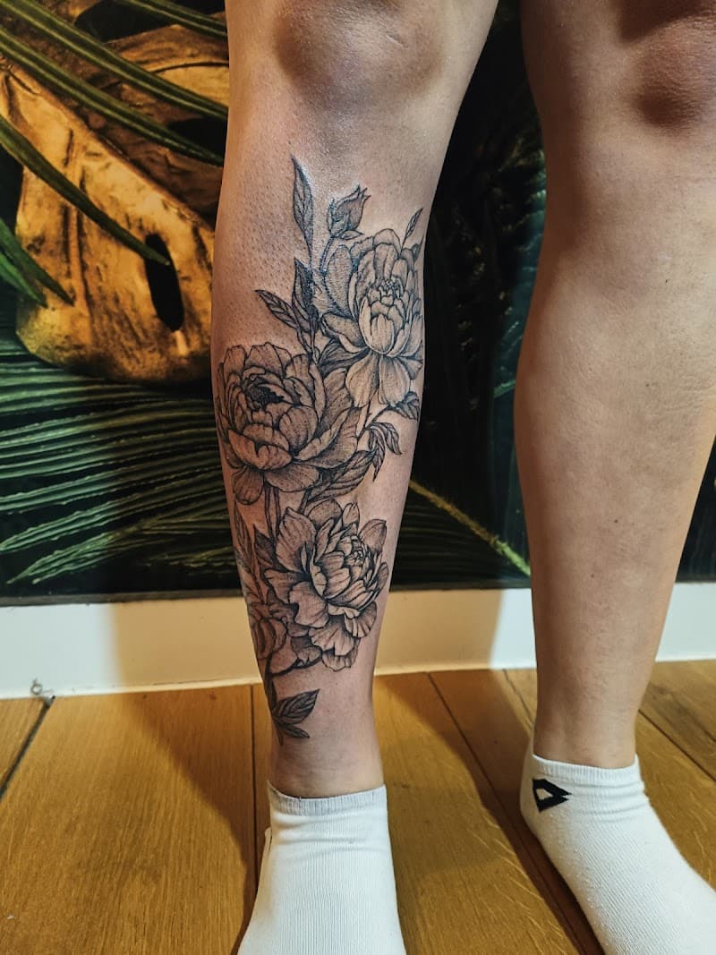 Zwart-grijze pioenrozen tattoo op onderbeen.