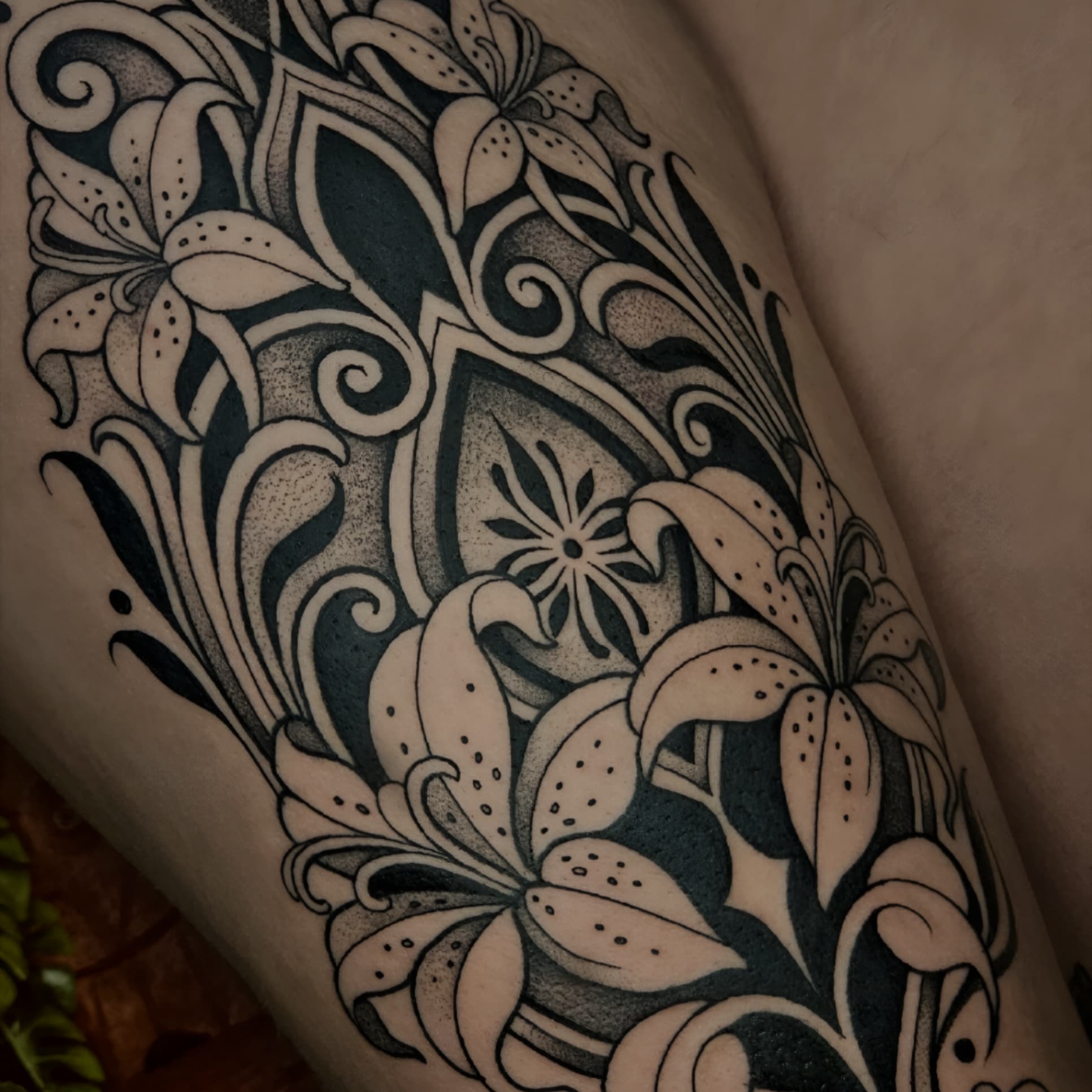 Grote blackwork tattoo van lelies en ornamenten op bovenbeen.