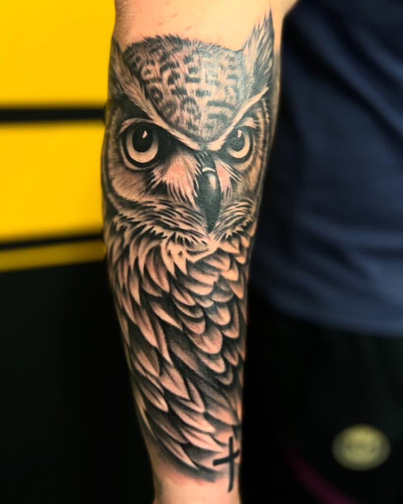 Realistische zwart-wit uil tattoo op de onderarm.