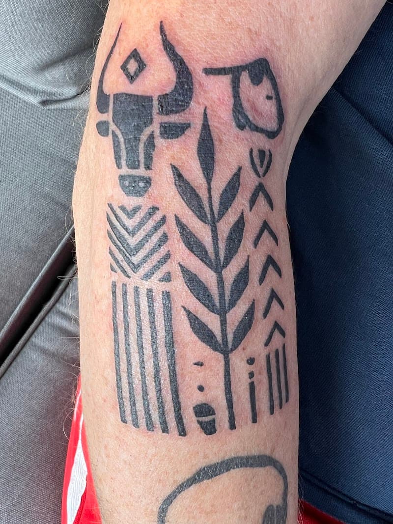 Zwart-wit tattoo met stier, plant en geometrische patronen op de onderarm.