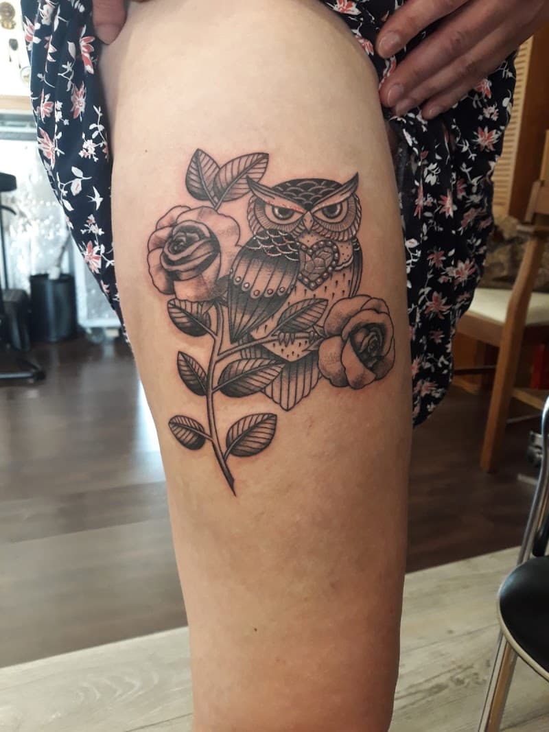 Zwart-wit tattoo van een uil op een tak met twee rozen op het bovenbeen.